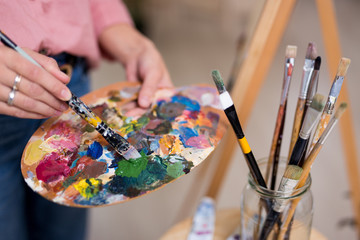 female hands holding paintbrush and palette with acrylic paints