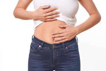 Woman with her monthly menstrual pains clutching her stomach with her hands as she becomes stressed by the ongoing cramps, torso view of her hands and tummy isolated on white