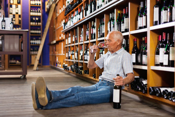Portrait of senior man sitting on floor in winery tasting room, drinking red wine