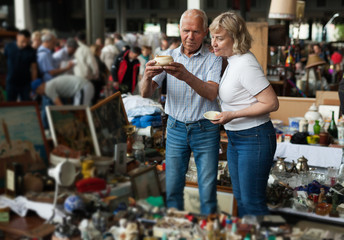Fototapeta na wymiar Glad man and woman choosing interesting souvenirs at traditional flea market