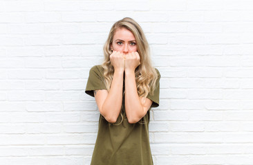 young blonde woman looking worried, anxious, stressed and afraid, biting fingernails and looking to...
