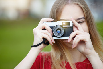 pretty cheerful smiling young woman holding old retro film camera and taking pictures, copy space, amateur photographer, sunny summer