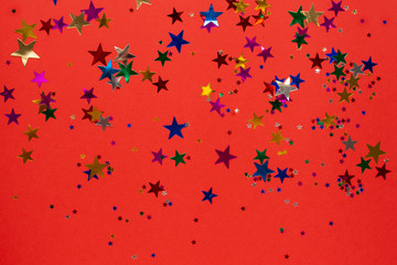 Colored stars confetti on red color paper background, christmas and new year concept