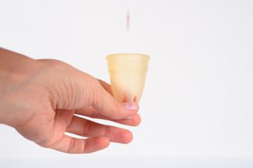 woman hand holding menstrual cup with blood on white background