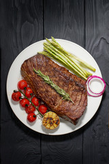 Barbecued Steak on a plate Served with asparagus and Tomatoes. Dark background, top view, horizontal photo