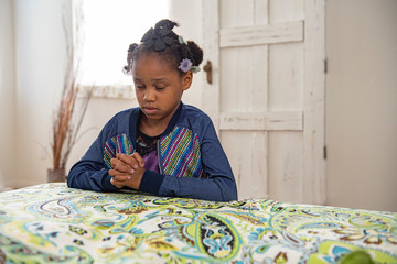 African American girl prays by the side of her bed. 