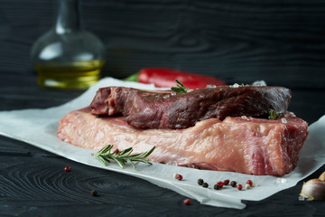 Raw fresh meat on paper with herbs, pepper and garlic on dark background