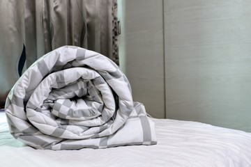 Fototapeta na wymiar Blanket roll on the white spread of bed in bedroom, prepared to wash.