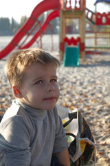 Little kid boy dreaming, pensive, on the beach near the water