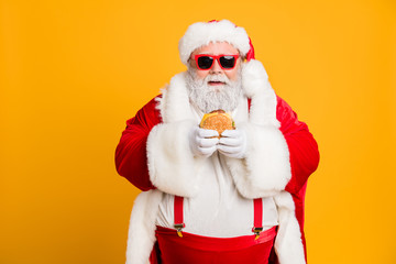 Portrait of funny funky fat santa claus dont care about health eat fast food big sandwich on x-mas tradition celebration wear style stylish suspenders isolated over shine color background