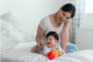 Obraz na płótnie Canvas Young beautiful asian mother with asian baby on bed and playing toy ball together on white bed with feeling happy and cheerful and the baby that crawling on the bed.Baby family concept