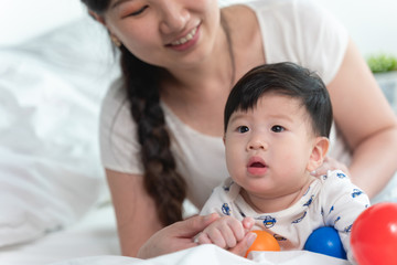 Obraz na płótnie Canvas Young beautiful asian mother with asian baby on bed and playing toy ball together on white bed with feeling happy and cheerful and the baby that crawling on the bed.Baby family concept