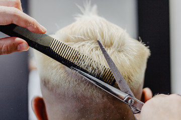 Close-up of the back of a client with dyed hair being cut by a hairdresser with a scissors and a hair comb