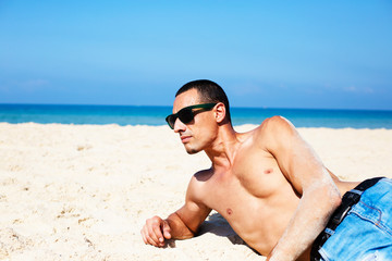 young muscular man resting and posing on the beach. 