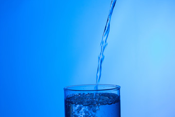 vaso lleno de agua en el que cae un chorro de agua externo produciendo un chapoteo y gotas que saltan fuera del vaso