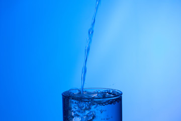 vaso lleno de agua en el que cae un chorro de agua externo produciendo un chapoteo y gotas que...