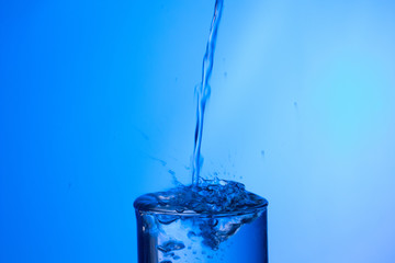 Chorro de agua llenando un vaso ya lleno y chapoteando y salpicando el agua que cae fuera del objeto de cristal