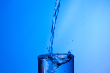 Chorro de agua llenando un vaso ya lleno y chapoteando y salpicando el agua que cae fuera del objeto de cristal
