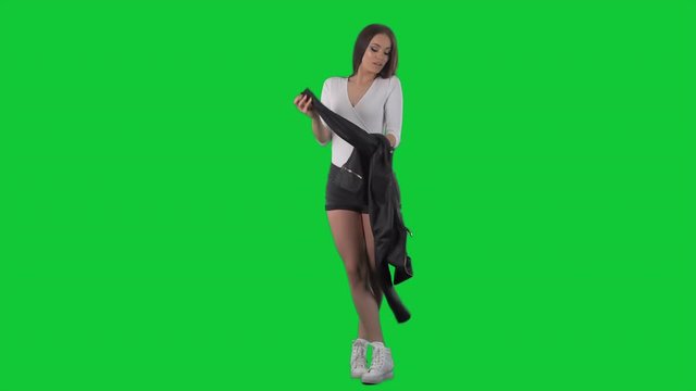 Gorgeous young brunette woman undressing and taking off her leather jacket.  Full body isolated on green screen chroma key background	