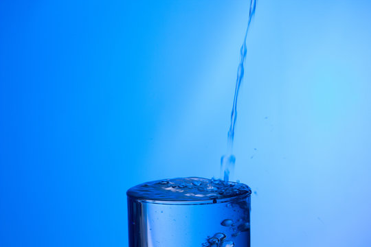 Agua entrando en un recipiente transparente de crital o pl&aacute;stico; agua salpicando 