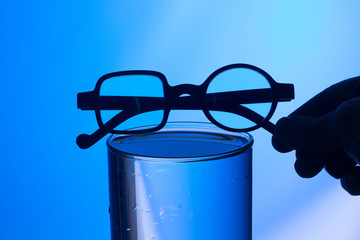Gafas en contraluz, encima de un vaso lleno de agua y sobre fondo azul