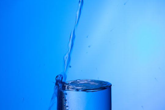 Agua entrando en un recipiente transparente de crital o pl&aacute;stico; agua salpicando 