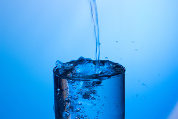 Agua cayendo en un vaso lleno produciendo chapoteo y que el agua sobresalga y caiga fuera mojñandolo todo