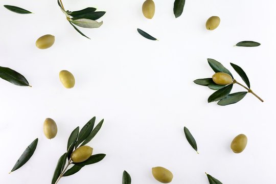 Frame or borders made of fresh green olive fruit with leaves on white background. Top view.