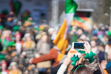 Hands of girl with mobile phone, making photo of carnival of St. Patrick's Day, traditional...