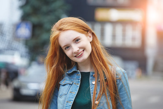candid outdoor portrait of pretty smiling young girl with long red hair, morning sunrise light