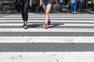 Pedestrian crossing city downtown women walk in motion on road. Many legs, feet and shoes from different people walking on town street crosswalk in a hurry pace urban day lifestyle. Large copyspace