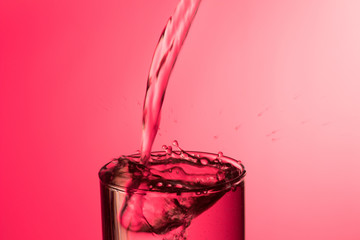 Chorro de agua llenando y rebosando un vaso de agua de cristal o plástico transparente sobre fondo rojo