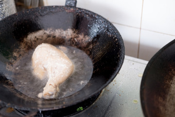 A piece of chicken fillet is fried in vegetable oil in a frying pan.