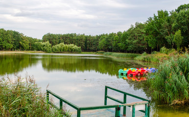 Beautiful lake park, colored old vintage plastic catamarans and boats near a wooden pier on the...