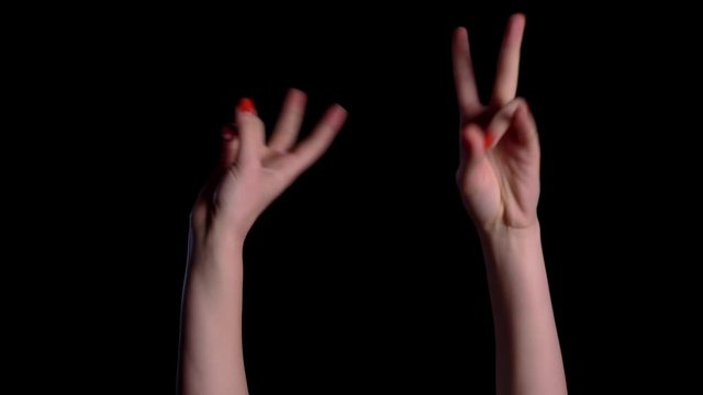 Two hands show a gesture of peace over black background in studio.