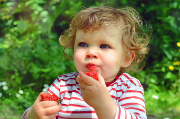 beautiful little girl enjoying strawberries in the garden