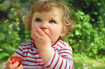 beautiful little girl enjoying strawberries in the garden