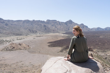 Happy tourist sitting in a rock of a viewpoint,with observation and relax in a volcanic desert at 