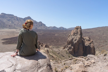 Happy tourist sitting in a rock of a viewpoint,with observation and relax in a volcanic desert at "Llano de Ucanca" in Tenerife, Canary Islands. Arid volcano crater and geological erosion land.