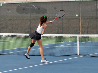 Young girl serving and volleying the ball during a tennis match