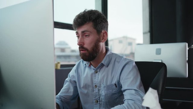 Unhealthy young business man workaholic working in the office sneezing allergy suffering cold or flu sitting at desk. Sickness. Medical concept.