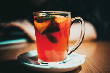 transparent cup with fruit tea, slices of lemon, orange and mint. A cup of tea is on a wooden table in a cafe. The concept of a cozy time in the autumn.