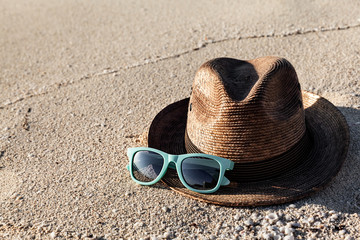 Brown straw hat and summer sunglasses on a sandy beach at sunny day