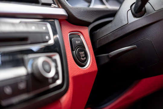 Close-up, isolated image of an engine Start Stop button seen on the dashboard of a german manufactured sports car, also showing its part red leather.
