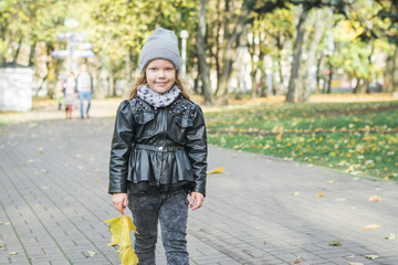 little girl walks in autumn park in warm clothes