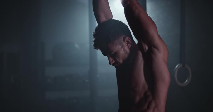 Athletic guy with perfect body in a cross fitness class have a hard workout training in a dark class in front of the camera