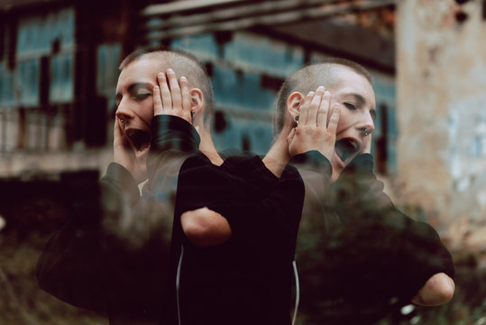 Reflected Crazy Female With Short Hair Keeping Hands Near Face And Shouting Loudly While Standing On Blurred Background Of Grungy Street