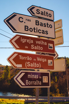 Direction arrows with foreign writings on signpost against wonderful autumn nature and cloudless blue sky on sunny day