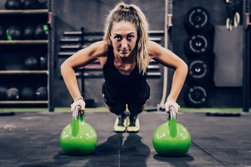 Muscular woman on hands in dumbbells in modern gym on blurred background