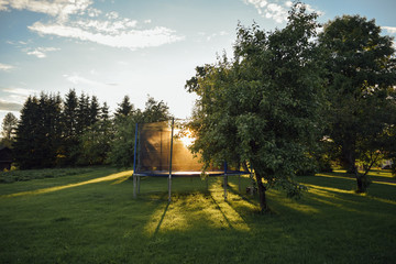 Open children's jump trampoline in the sun on green grass in the yard of finnish house with trees,...